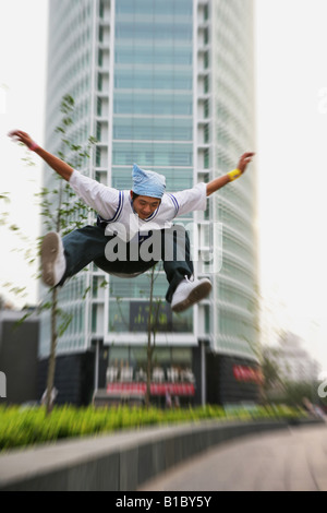 Jeune homme sautant sur square à côté d'immeubles de bureaux,Beijing, Chine Banque D'Images