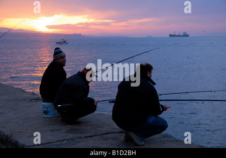 Trois pêcheur leur commerce comme le soleil se lève sur le Bosphore au début de l'hiver un matin à Istanbul, Turquie. Banque D'Images