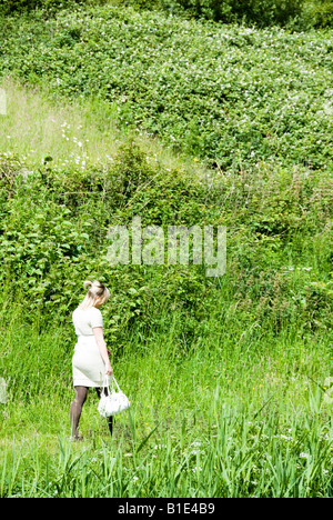 Une adolescente blonde marche à travers les fleurs sauvages et les herbes hautes Banque D'Images