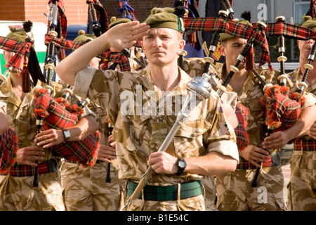 Soldats écossais pipe major saluant avant de battre la retraite avec cornemuse en uniforme militaire derrière fatigues du désert Banque D'Images