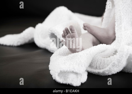 Les pieds de nouveau-né qui sort de sous un manteau blanc portant sur le canapé en cuir noir Causasian Alaska United States Banque D'Images