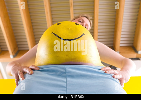 Smiley jaune peint sur le ventre de femme enceinte comme elle se tient avec les mains sur ses hanches l'Alaska, United States Banque D'Images