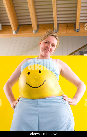 Smiley jaune peint sur le ventre de femme enceinte comme elle se tient avec les mains sur ses hanches l'Alaska, United States Banque D'Images