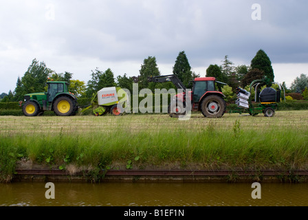 Tracteur John Deere vert tirant une ramasseuse-presse à balles rondes McCormick rouge tirant une Balw emballage dans un champ pendant la fenaison Cheshire Banque D'Images