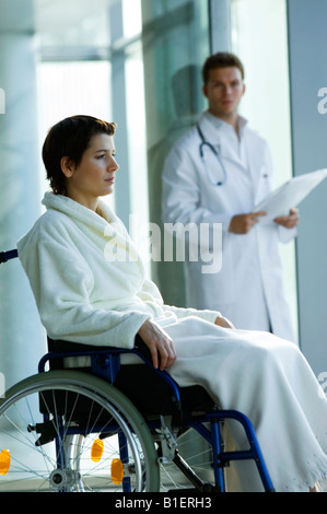 Femme assise dans un fauteuil roulant et d'un médecin homme debout dans l'arrière-plan Banque D'Images