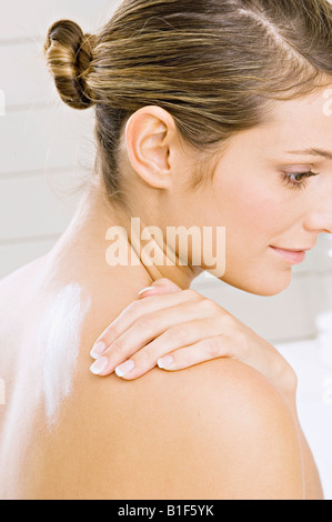 Portrait of a young woman applying moisturizer sur son épaule Banque D'Images