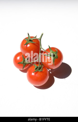 Plusieurs tomates cerises rouges avec stork vert sur fond blanc studio Banque D'Images