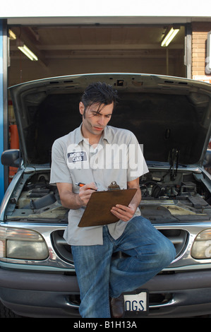 Mechanic writing on clipboard par ouvrir un capot de voiture Banque D'Images