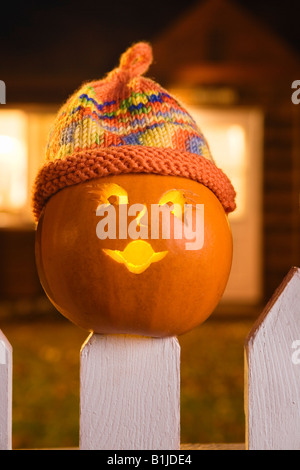 Jack-O-Lantern face portant un chapeau bas coincé au sommet d'un piquet de clôture blanche picktet au crépuscule au cours de l'automne Banque D'Images