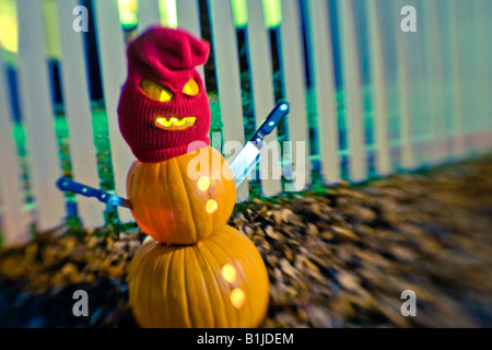 Burgler Jack-O-Lantern homme debout portant un masque d'ensemencement avec couteaux steak comme les bras en avant d'un picktet white fence Banque D'Images