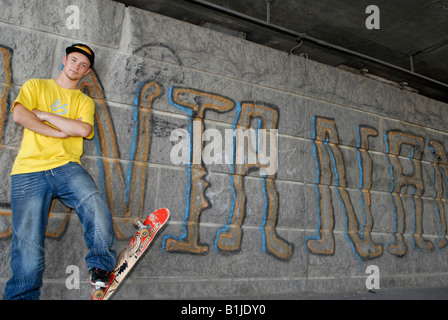 Adolescent mâle debout devant un mur avec son skateboard Banque D'Images