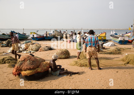 Un homme raccommode les filets de pêche. Bateaux de pêche sur la plage de sable près de Kollam Thangasseri au Kerala, en Inde. Banque D'Images