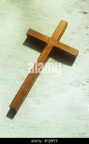 Close up of small crucifix en bois simple couché dans la lumière du soleil sur le rebord de pierre brute peint crème ou de niche Banque D'Images