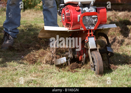 L'homme portait un jean et des chaussures de sécurité fonctionne jardin à essence rotavator utilisé pour battre le sol de un jardin newtownabbey Banque D'Images