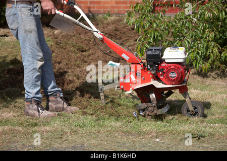 L'homme portait un jean et des chaussures de sécurité fonctionne jardin à essence rotavator utilisé pour battre le sol de un jardin newtownabbey Banque D'Images