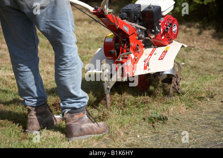 L'homme portait un jean et des chaussures de sécurité fonctionne jardin à essence rotavator utilisé pour battre le sol de un jardin newtownabbey Banque D'Images
