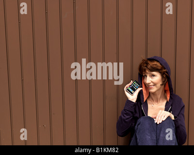 Senior woman with iPhone portant un 'hoody' assis à la porte du garage. Banque D'Images