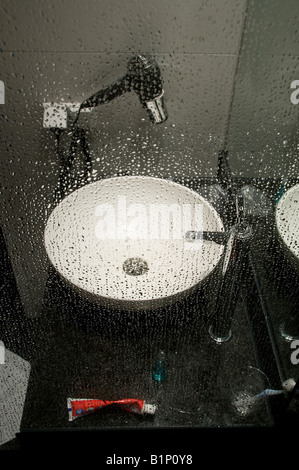 Une salle de bains moderne avec un évier de navire vu à travers une vitre recouverte de gouttelettes d'eau. Banque D'Images