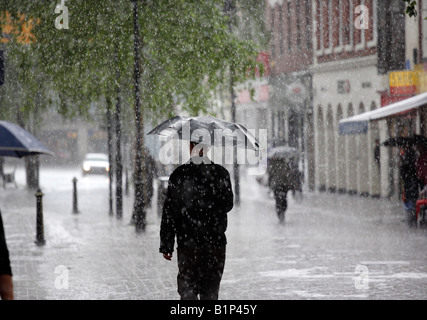 Un homme tenant un parapluie en marchant le long de High Street dans le Worcestershire Bromsgrove UK pendant une tempête de pluie Banque D'Images