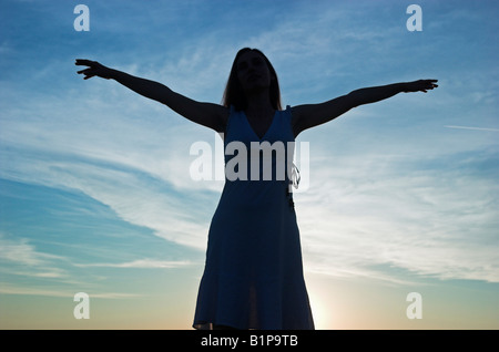 Silhouette d'une jeune femme à la tombée du soleil derrière les bras levés Banque D'Images