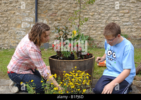 Les élèves du secondaire planter des fleurs en pots en bois ronde à un projet de jardin communautaire Banque D'Images