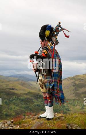 Piper écossais jouer de la cornemuse et portant sur kilt en tartan hill-tops de Invernesshire, Scotland UK Banque D'Images