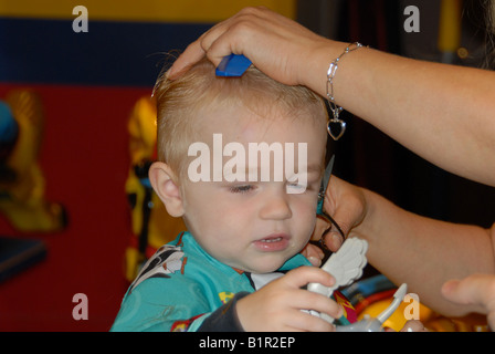 Un bambin se prépare pour sa première coupe de cheveux dans un salon de coiffure. Banque D'Images