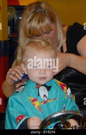 Un bambin se prépare pour sa première coupe de cheveux dans un salon de coiffure. Banque D'Images