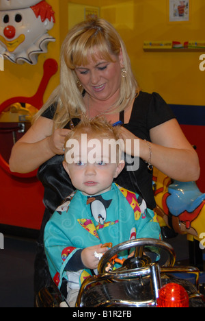 Un bambin se prépare pour sa première coupe de cheveux dans un salon de coiffure. Banque D'Images