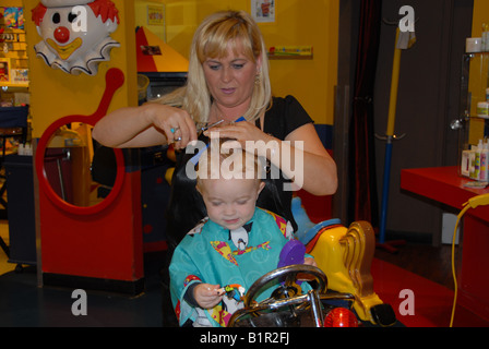 Un bambin se prépare pour sa première coupe de cheveux dans un salon de coiffure. Banque D'Images