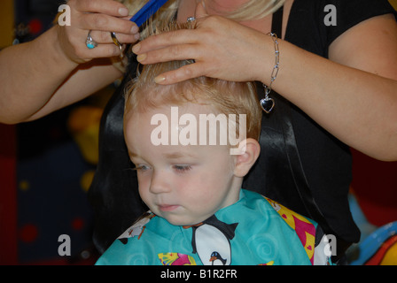 Un bambin se prépare pour sa première coupe de cheveux dans un salon de coiffure. Banque D'Images