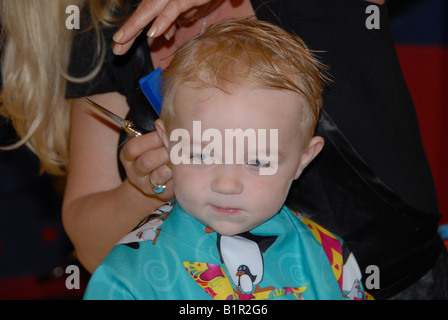 Un bambin se prépare pour sa première coupe de cheveux dans un salon de coiffure. Banque D'Images