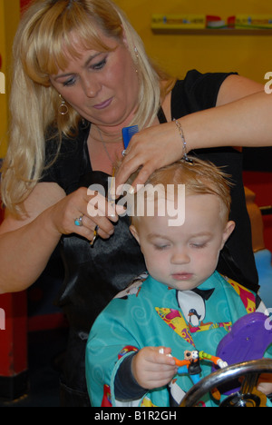 Un bambin se prépare pour sa première coupe de cheveux dans un salon de coiffure. Banque D'Images