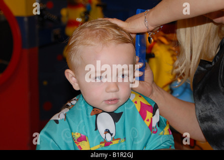 Un bambin se prépare pour sa première coupe de cheveux dans un salon de coiffure. Banque D'Images