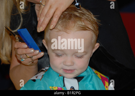 Un bambin se prépare pour sa première coupe de cheveux dans un salon de coiffure. Banque D'Images