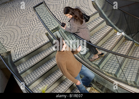 Un jeune homme et femme sont croisaient sur un escalier à main transportant des appareils informatisés. Banque D'Images