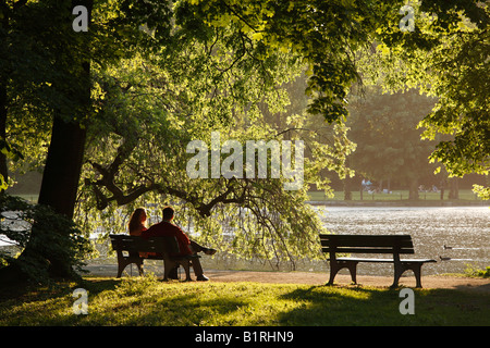 Couple assis sur un banc de parc en anglais Garten, jardin anglais au lac Kleinhesseloher See, Munich, Haute-Bavière, Ger Banque D'Images