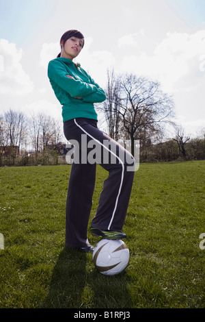 Jeune femme à la recherche dans l'appareil photo avec les bras croisés et un football sous son pied Banque D'Images