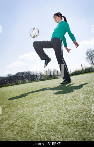 Jeune femme jouant au football sur un terrain de sport Banque D'Images
