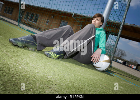 Jeune femme avec un football appuyé contre un objectif Banque D'Images