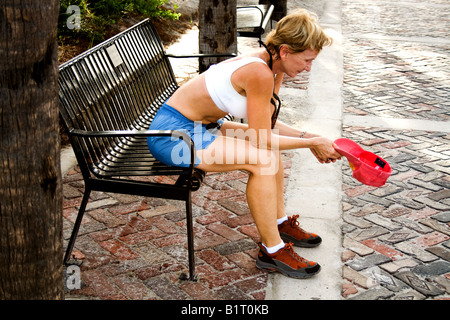 Femme d'âge moyen au repos de l'athlète avec le chapeau à la main sur un banc à Atlantic Beach, en Floride Banque D'Images