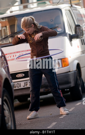 Teenage Girl Playing with hula hoop hoolah dans la rue devant sa maison, debout entre les voitures en stationnement, la sécurité routière s'inquiéter, UK Banque D'Images