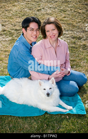 Deux jeunes mariés homme asiatique avec des lunettes et enceinte Caucasian woman posing together avec leur chien Banque D'Images