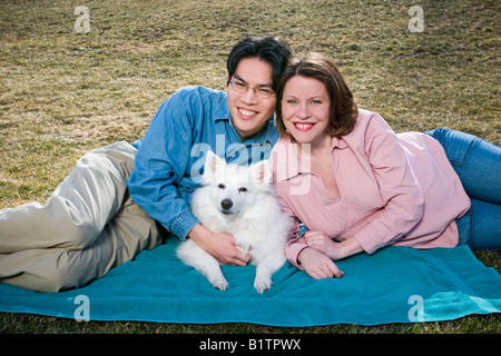 Deux jeunes mariés homme asiatique avec des lunettes et enceinte Caucasian woman posing together avec leur chien Banque D'Images