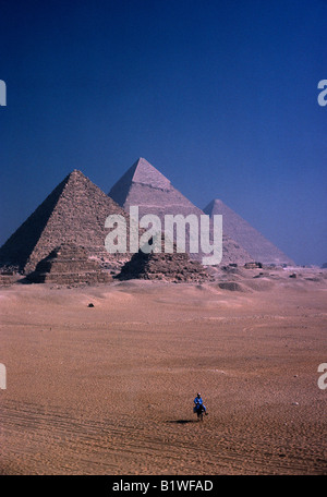 Egypte Afrique du Nord Moyen-orient Le Caire Les pyramides de Gizeh, avec l'homme sur l'âne en premier plan équitation à travers les sables du désert Banque D'Images
