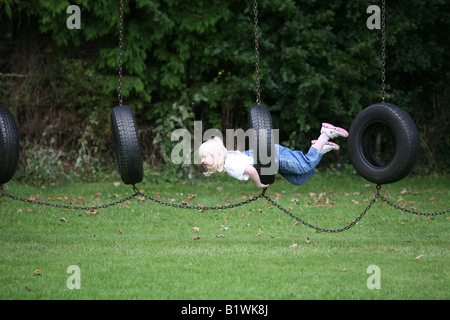 Jeune fille blonde jouant sur les pneus de rotation dans l'aire de jeux. Banque D'Images