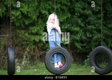 Jeune fille blonde jouant sur les pneus de rotation dans l'aire de jeux. Banque D'Images