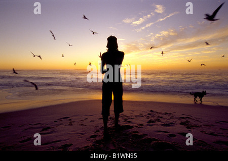 Une jeune femme regarde le coucher du soleil sur la mer à la plage de Camps Bay, Cape Town Afrique du Sud Banque D'Images
