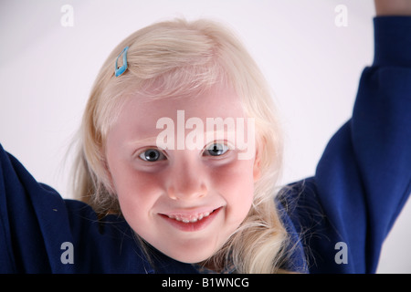 Petite fille de l'école d'une chevelure de blonde s'étend ses bras au-dessus de sa tête contre un fond blanc Banque D'Images