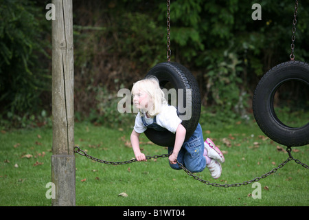 Jeune fille blonde jouant sur les pneus de rotation dans l'aire de jeux. Banque D'Images